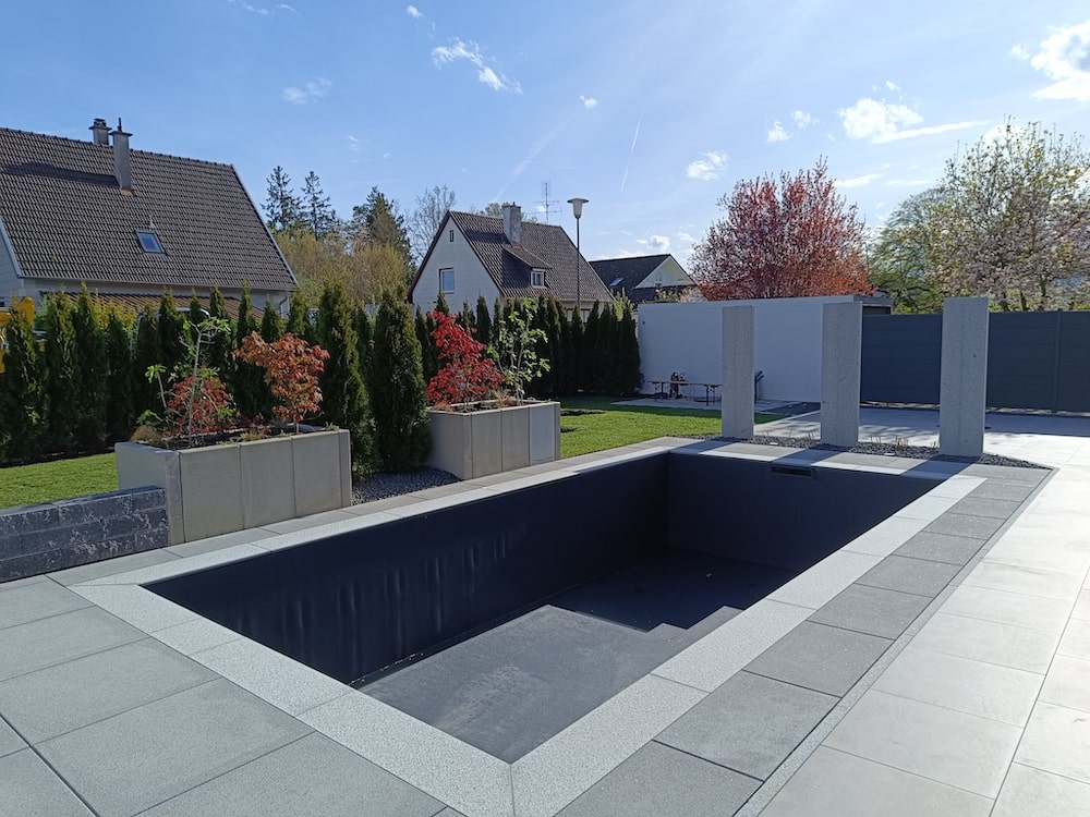 Gartenanlage, eine Gartenoase mit großen grauen Bodenplatten, die einen leeren Pool umrahmen