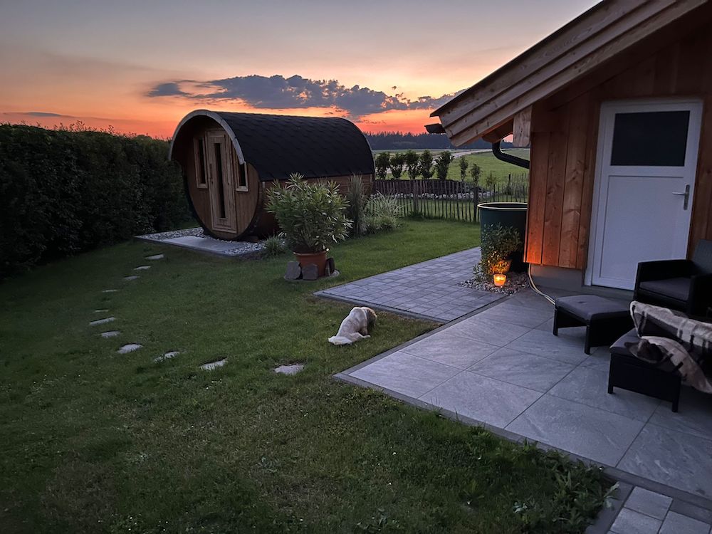 Rundholzsauna im grünen Garten neben dem Gartenhaus mit gepflasterter Terrasse